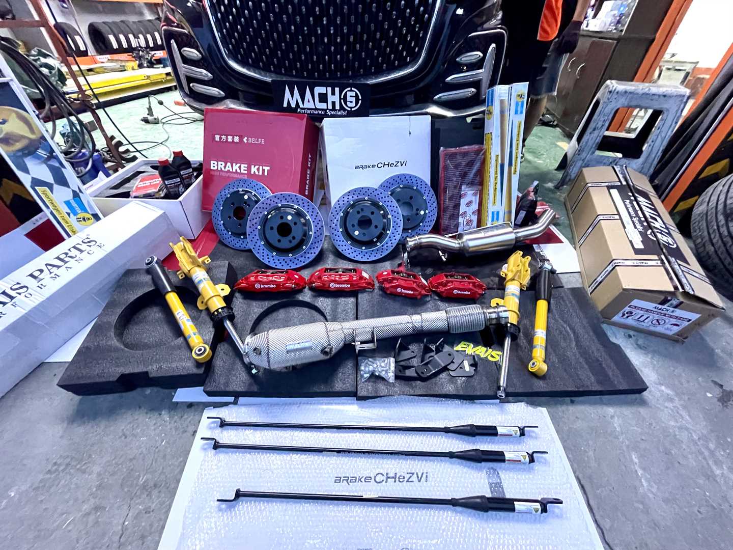 A family photo of the V260 before performance modifications, including KW coilovers, brake discs, stabiliser bars, BMC air filter, and other components. Brand names are featured, published by Mach5 Performance.